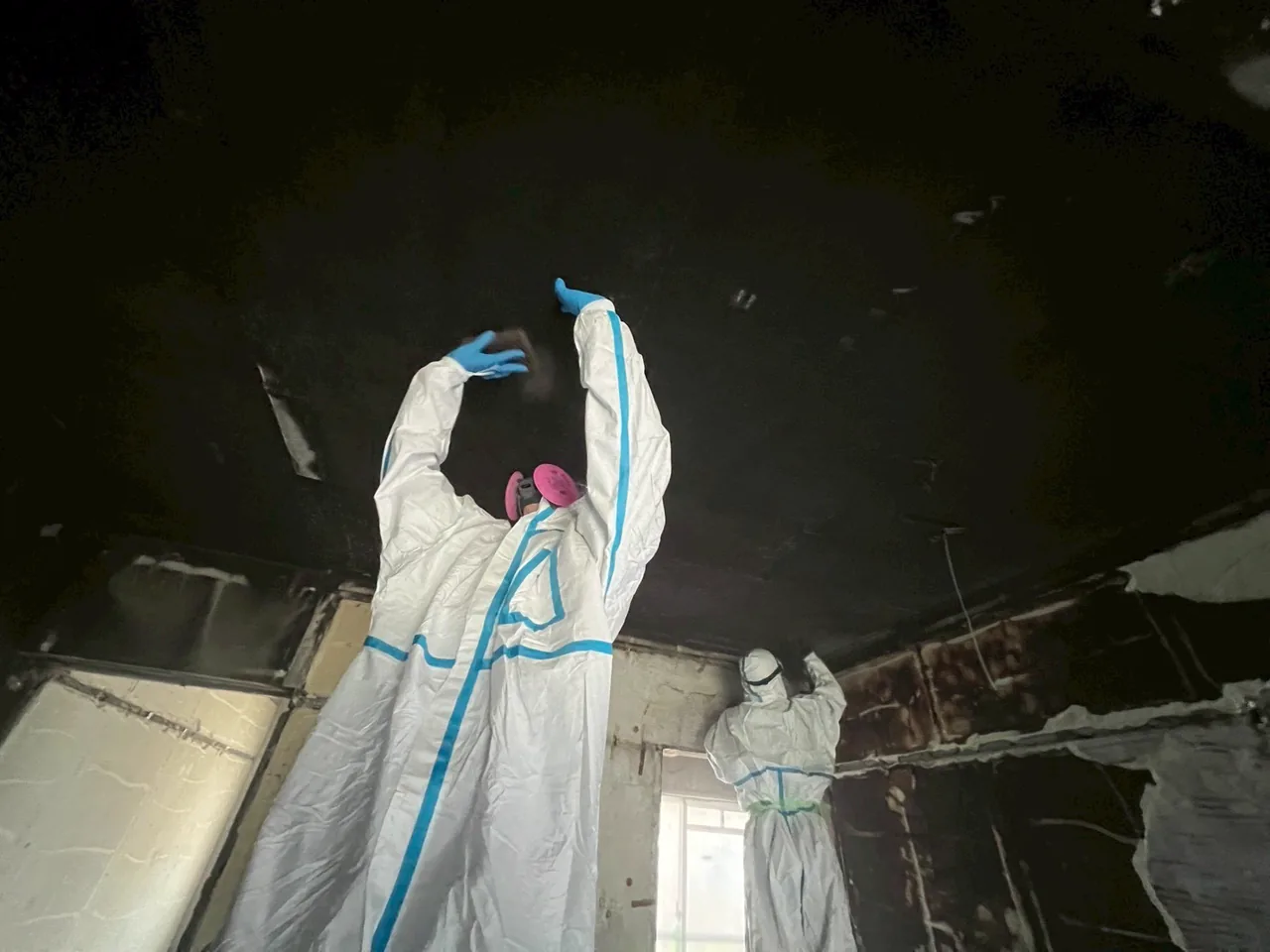 防護装備の作業員が煤けた天井に手を伸ばして作業する様子